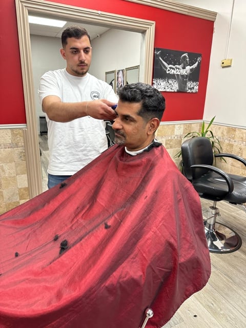 Barber cutting clients hair in salon with red walls and mirror