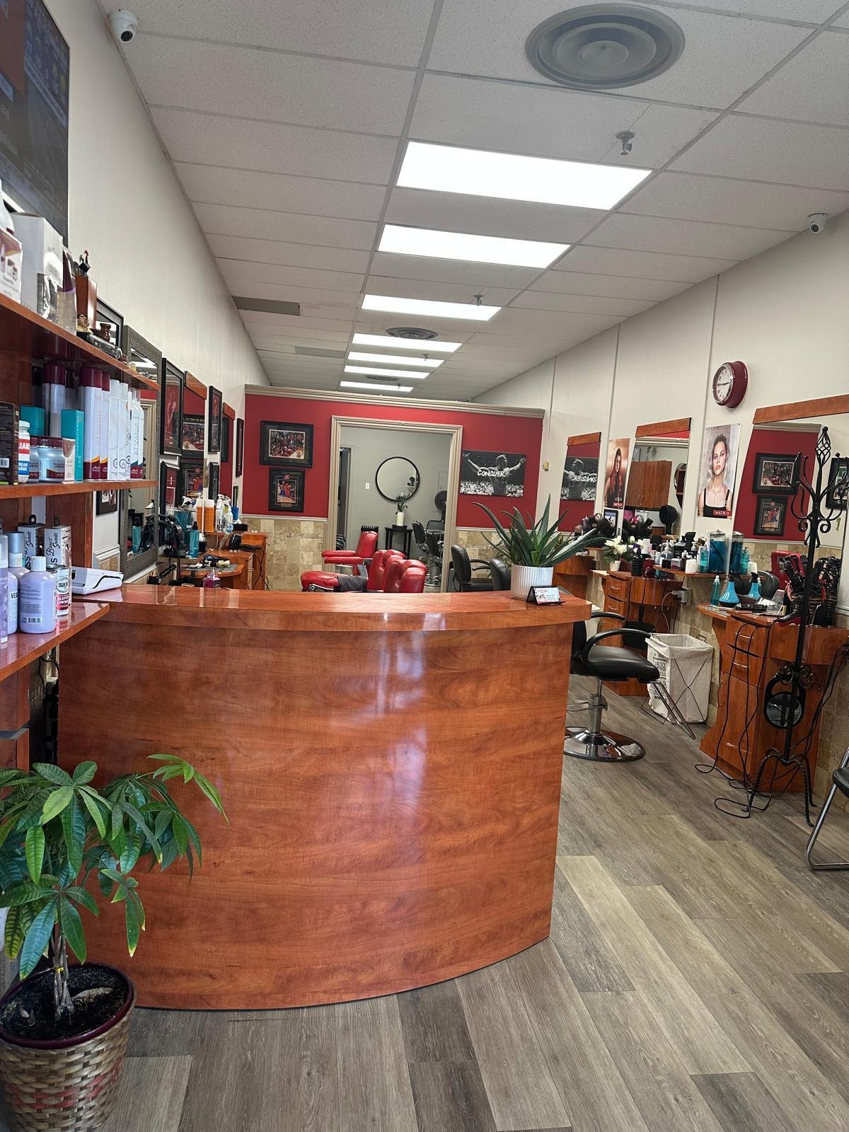Interior of a hair salon with a curved wooden reception desk, red accent walls, product shelves, and styling stations with mirrors