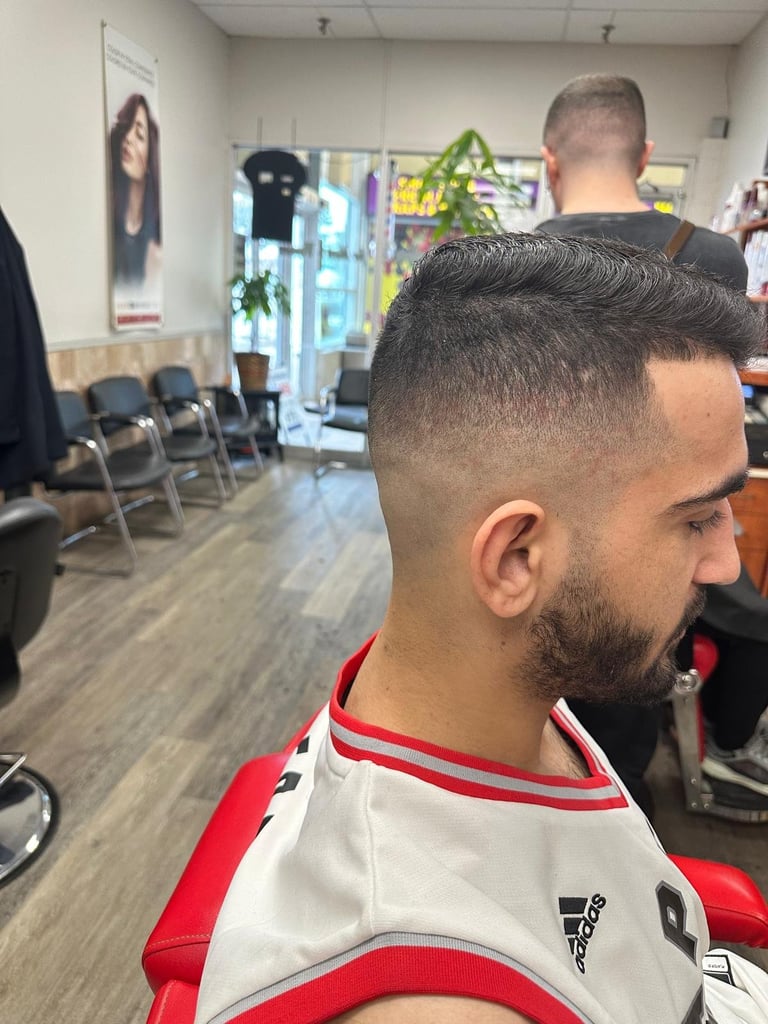 Man with fade haircut and beard in barber shop, wearing red and white shirt, viewed from side profile
