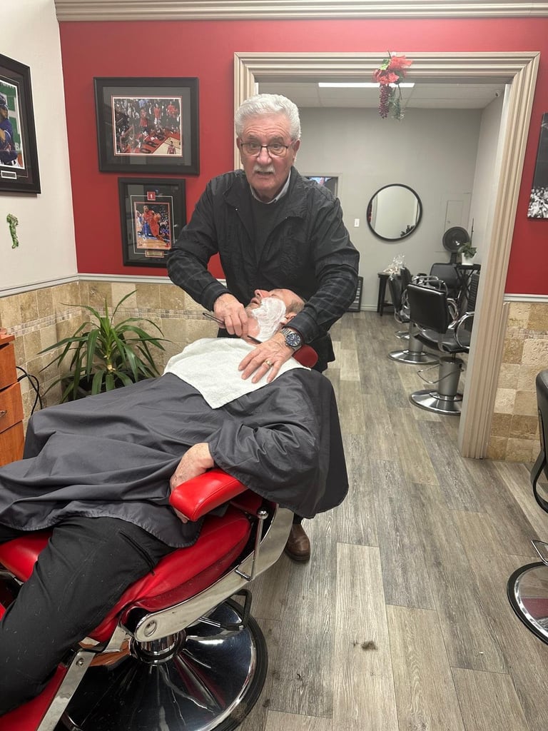 Older man with glasses styling hair of a client seated in a barber chair in a salon with red walls and framed photos