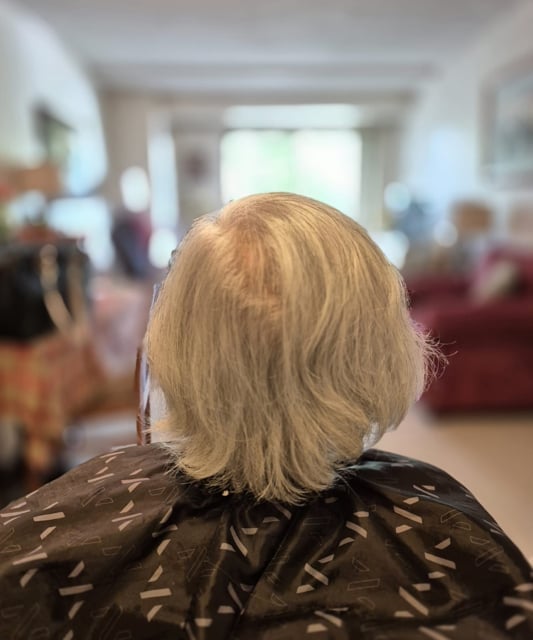 Back view of a person with short blonde hair wearing a dark patterned shirt in an indoor setting