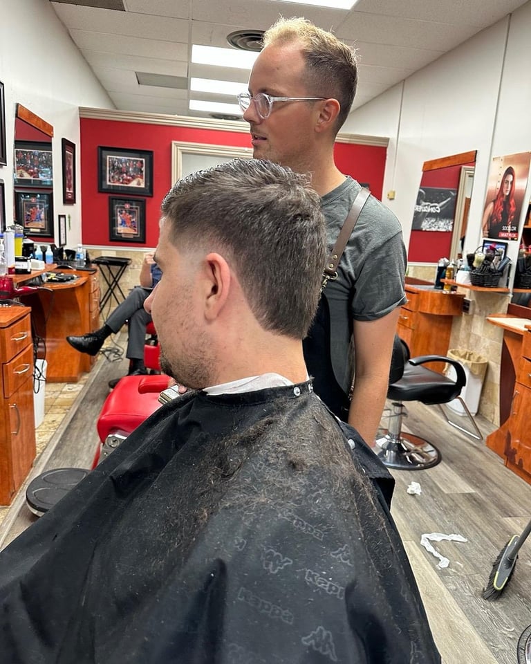 Barber cutting a customers hair in a salon with red and white walls and photos displayed